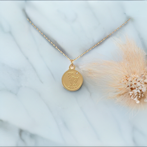 Gold Aries Medallion Necklace on a marble-like platform next to a dry flower