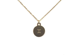 A zodiac symbol on the back side of a gold Gemini Zodiac Coin Necklace on a white ground.