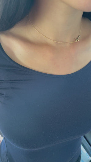 A gold sideway cross choker necklace in 14k gold is worn on a model. 