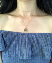 Load image into Gallery viewer, A gold Capricorn Zodiac Sign Necklace , worn on a model , showing the front side of the medallion necklace.
