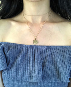 A gold Capricorn Zodiac Sign Necklace , worn on a model , showing the front side of the medallion necklace.