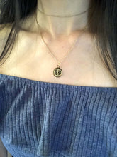 Load image into Gallery viewer, The Gemini Zodiac Sign necklace features a gold disc adorned with a design resembling the faces of two women looking at each other, as showcased on a model. 
