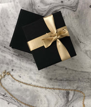 Load image into Gallery viewer, Gift Wrap Packaging ( black box with gold ribbon) next to a gold necklace on a marble like background
