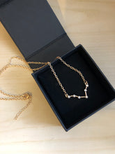 Load image into Gallery viewer, A gold Pisces Zodiac Sign Necklace in a black jewelry box on a wood-like background. 
