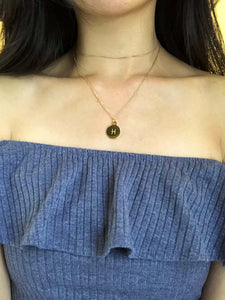 The back side of a gold Pisces Zodiac Sign necklace showcasing the Pisces symbol is worn on a model. 