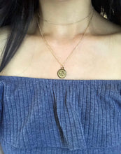 Load image into Gallery viewer, The front side of a gold Sagittarius Disc Necklace, paired with a dainty gold chocker, is worn on a model. 
