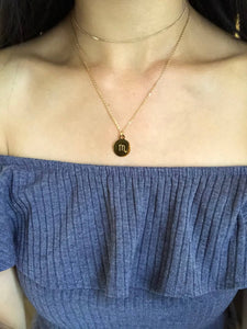 The back side of a gold Scorpio Symbol Necklace, paired with a gold dainty choker is worn on a model. 