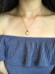 The front side of a gold Scorpio Disc Necklace, paired with a gold dainty choker is shown on a model. 