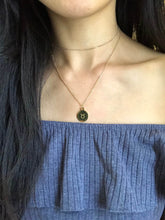 Load image into Gallery viewer, A gold Taurus Zodiac Sign Necklace that features a Taurus Symbol on the back side of the coin, paired with a gold dainty choker is worn on a model.
