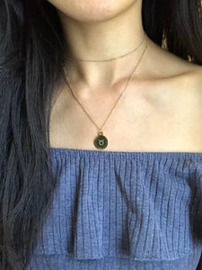 A gold Taurus Zodiac Sign Necklace that features a Taurus Symbol on the back side of the coin, paired with a gold dainty choker is worn on a model.