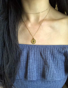 A gold Taurus Disc Necklace, paired with a gold dainty necklace is worn on a model. 